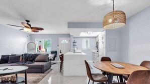 Eine moderne Küche mit Kochinsel, ein Essbereich mit Holztisch und Stühlen sowie ein Wohnzimmer mit Sofa und Couchtisch.