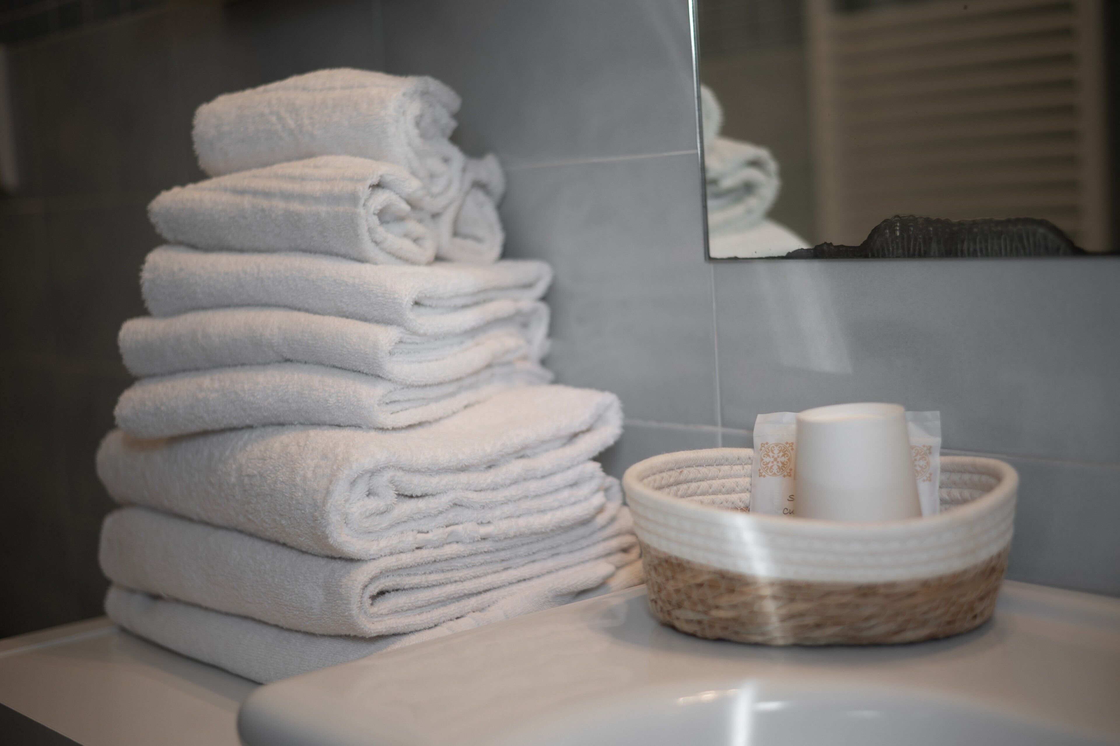 Une pile de serviettes blanches, un lavabo blanc et un panier tressé contenant des articles de toilette.