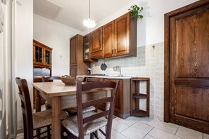 A kitchen with wooden cabinets, a dining table with chairs, a hanging light fixture, and a tiled backsplash. - Apartment 'Agriturismo Vallerana Il Noce' with Private Terrace, Wi-Fi and Air Conditioning (Capalbio)