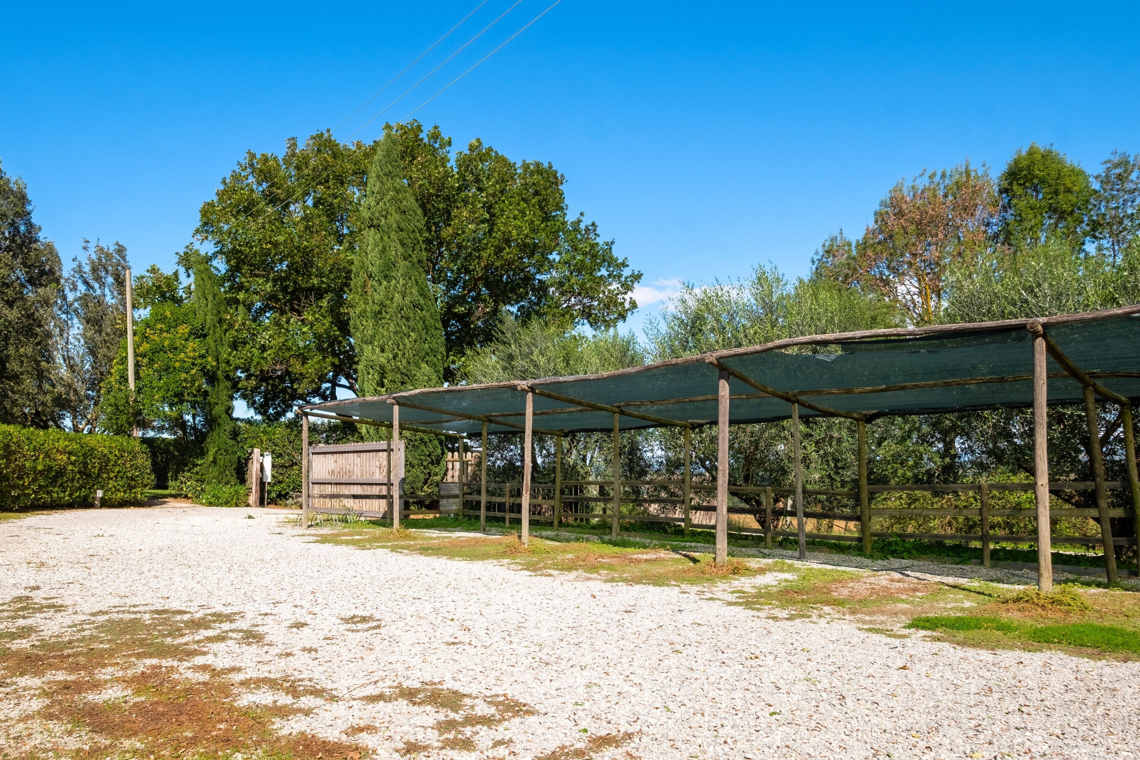 A covered outdoor area with a gravel path, surrounded by trees and a wooden fence.