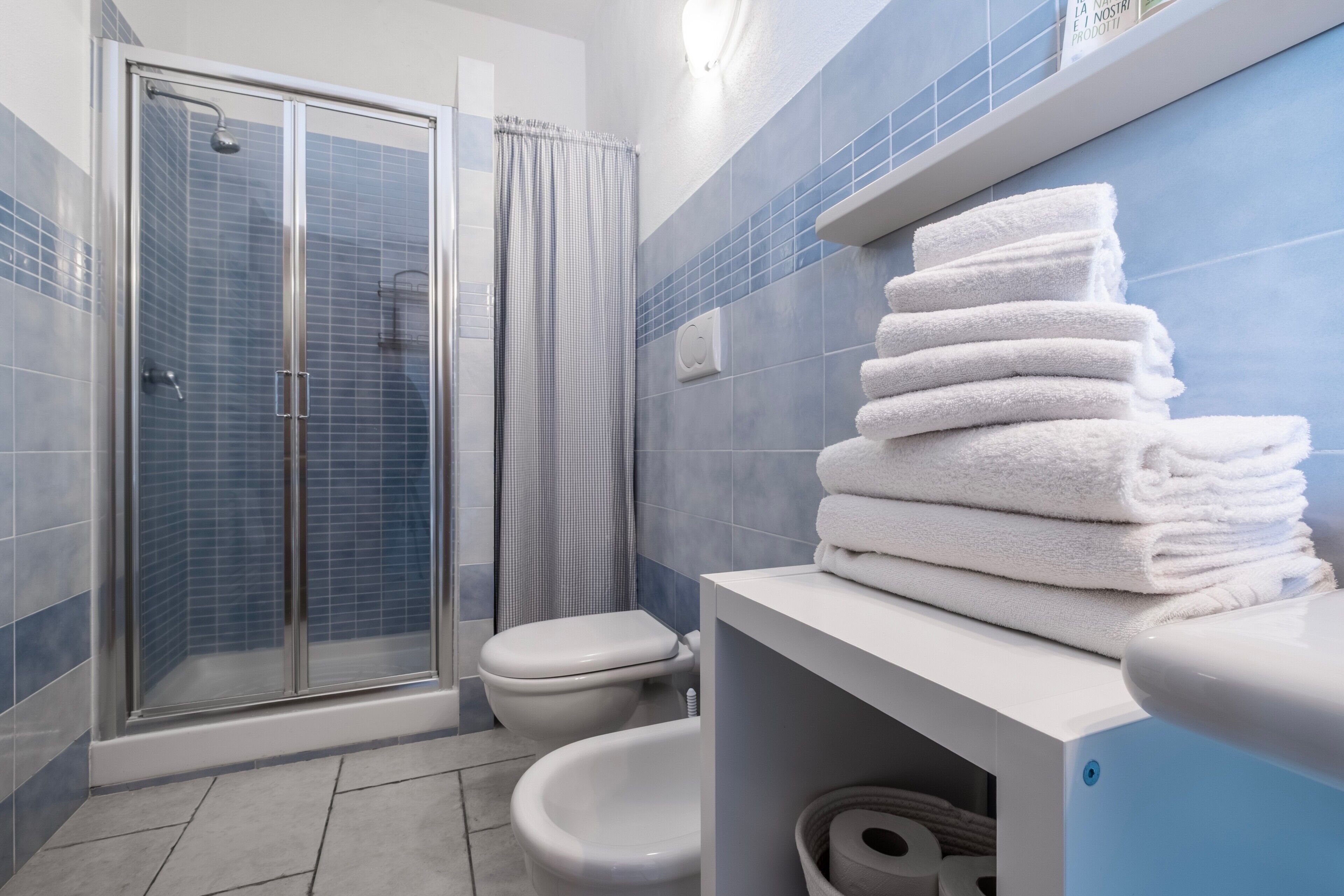 Un baño con cabina de ducha de vidrio, inodoro y una pila de toallas blancas en un mostrador.