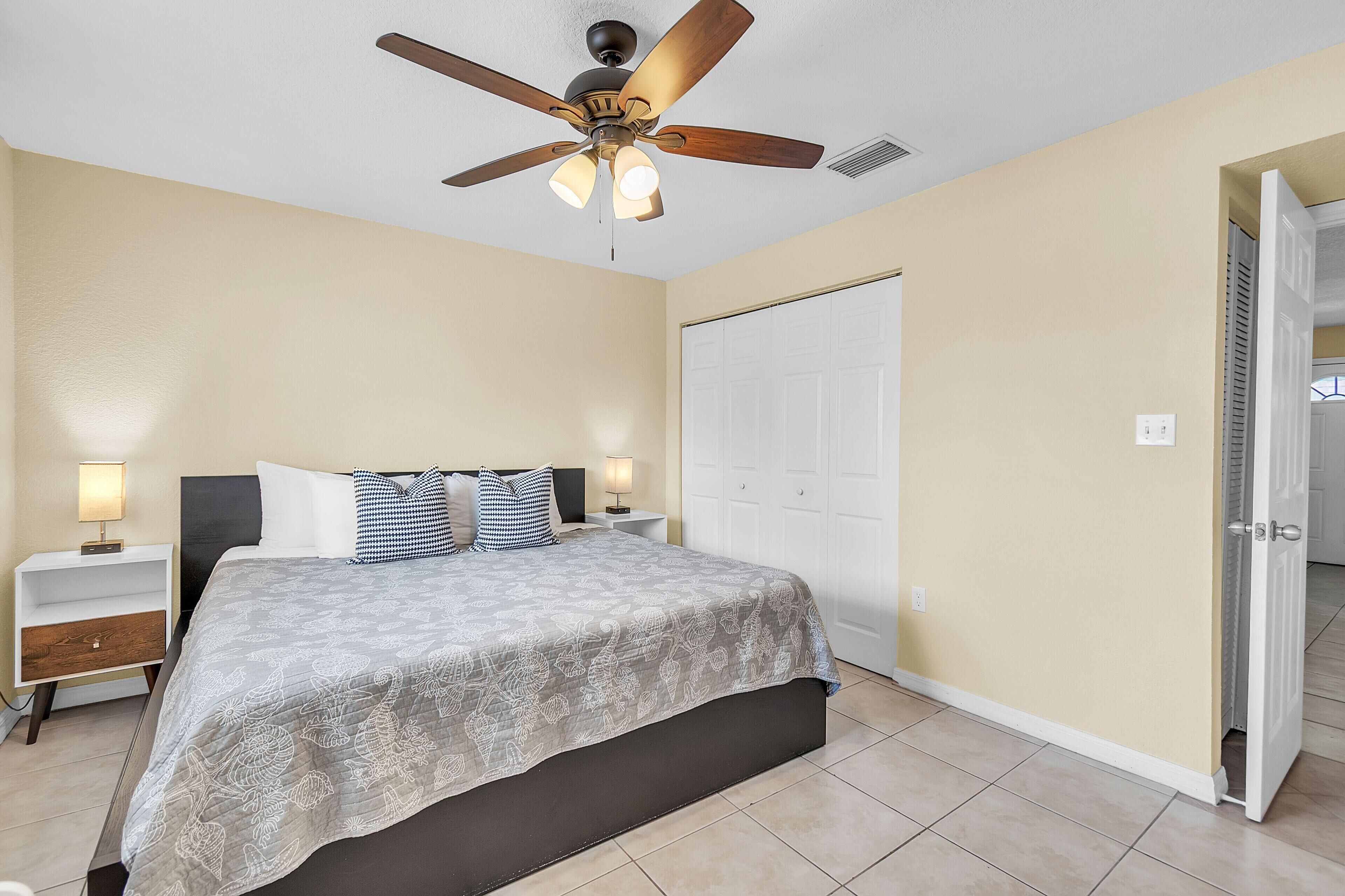 Une chambre à coucher comprenant un lit, des tables de chevet, un ventilateur de plafond et une armoire.