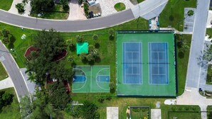 Vue aérienne d’un complexe sportif comprenant plusieurs courts de tennis, un terrain de basketball et des espaces verts environnants.