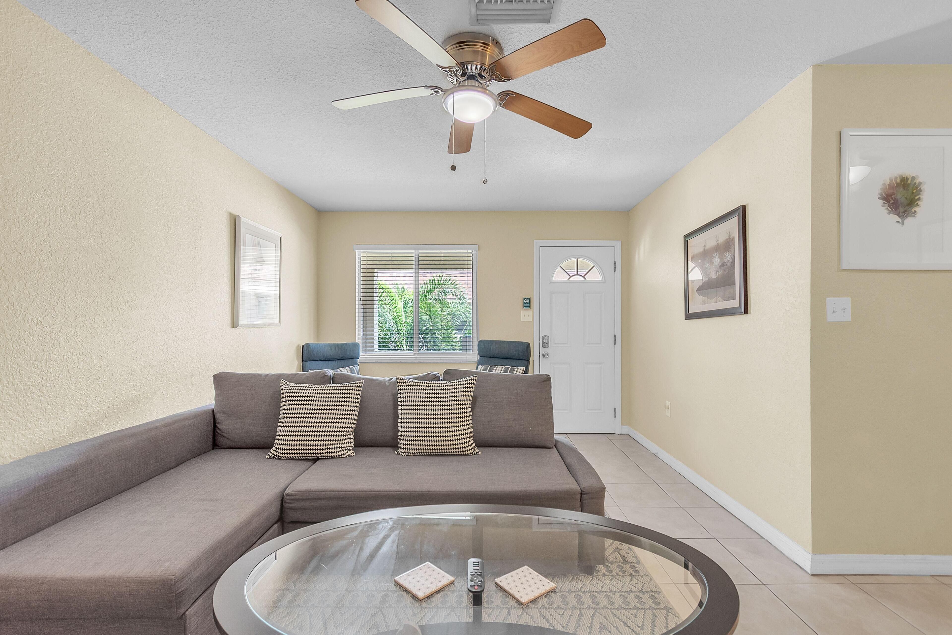 A living room with a sofa, a glass coffee table, and a ceiling fan.