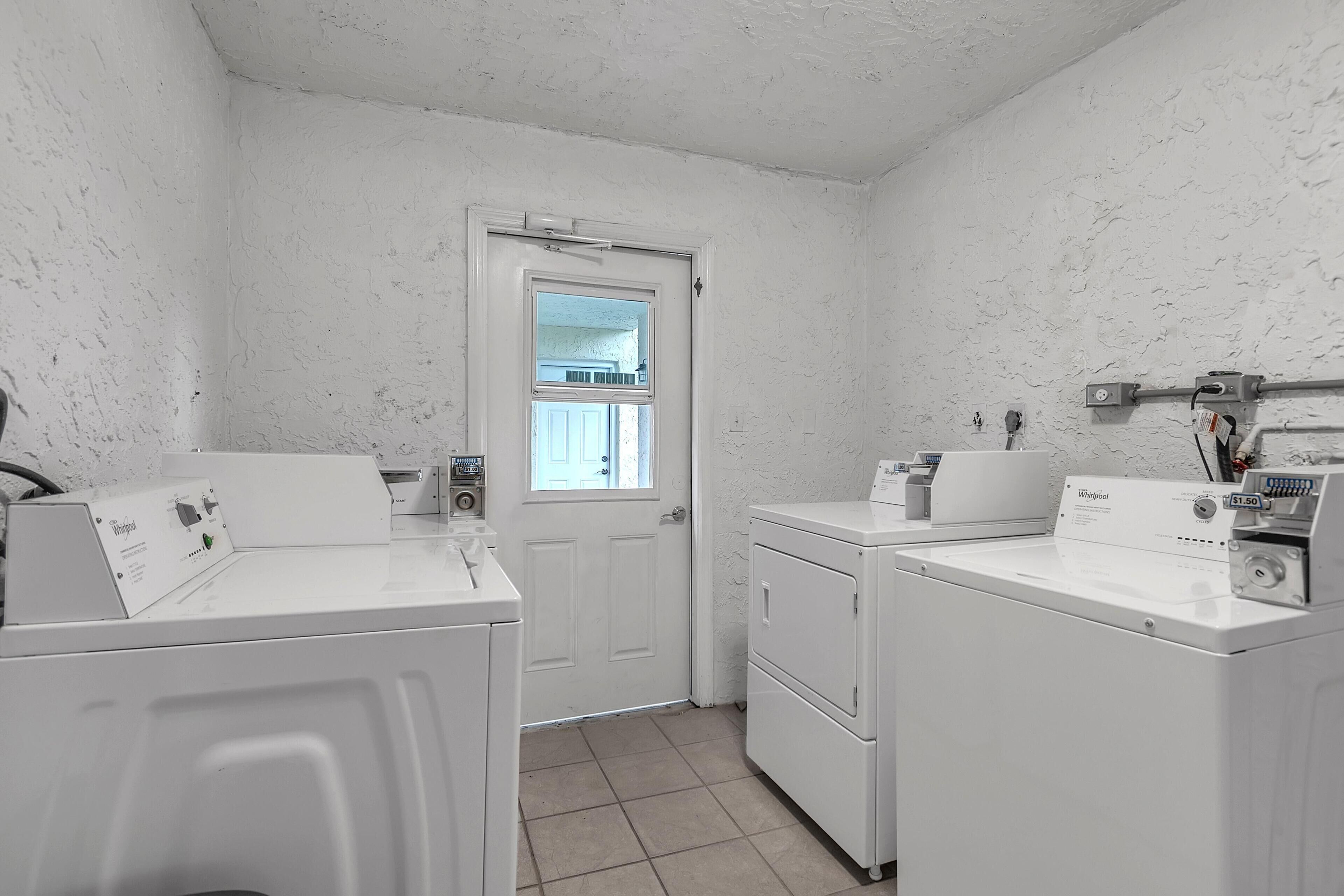 A laundry room with two front-loading washers and dryers, a window, and a door.