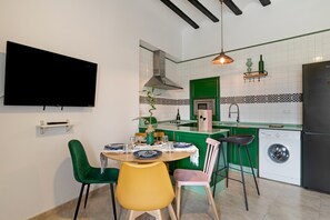 A modern kitchen with a dining area, green and white tiles, a flat-screen TV, and a washing machine.