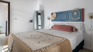 A bedroom with a bed, a mirror, a blue headboard, and a wall-mounted light fixture.