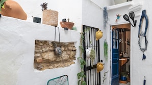 A narrow alleyway with a stone wall, a metal gate, and a blue door leading to a room.