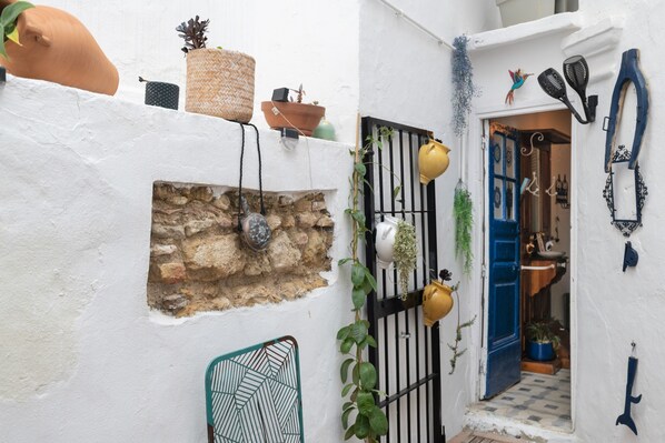 A narrow alleyway with a stone wall, a metal gate, and a blue door leading to a room.