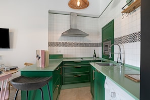 A kitchen with green cabinets, a stainless steel range hood, a microwave, and a sink.