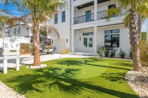 Un bâtiment moderne à deux étages, doté d’une pelouse bien entretenue, de palmiers et d’un véhicule utilitaire pour se déplacer sur un terrain de golf.