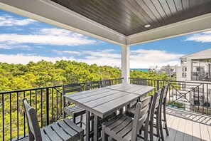 A covered outdoor area with a table and chairs, overlooking a lush green landscape and a body of water.