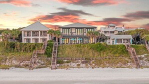 A beachfront property with multiple buildings, including a large house with a balcony and a smaller structure. There are wooden staircases leading to the beach, and the property is surrounded by vegetation and sand. - Seaside Serenity|Gulf Front|Private Beach Access|Private Pool (Seagrove Beach)
