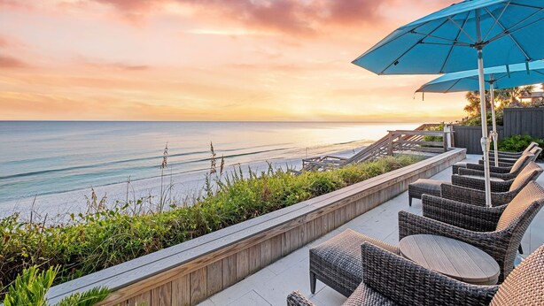A seaside patio with wicker furniture and a blue umbrella, overlooking the ocean. - Seaside Serenity|Gulf Front|Private Beach Access|Private Pool (Seagrove Beach)