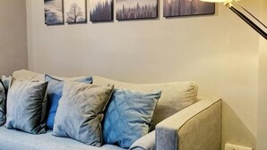 Een kamer met een lichtgekleurde bank, een wandlamp en vier ingelijste foto's.