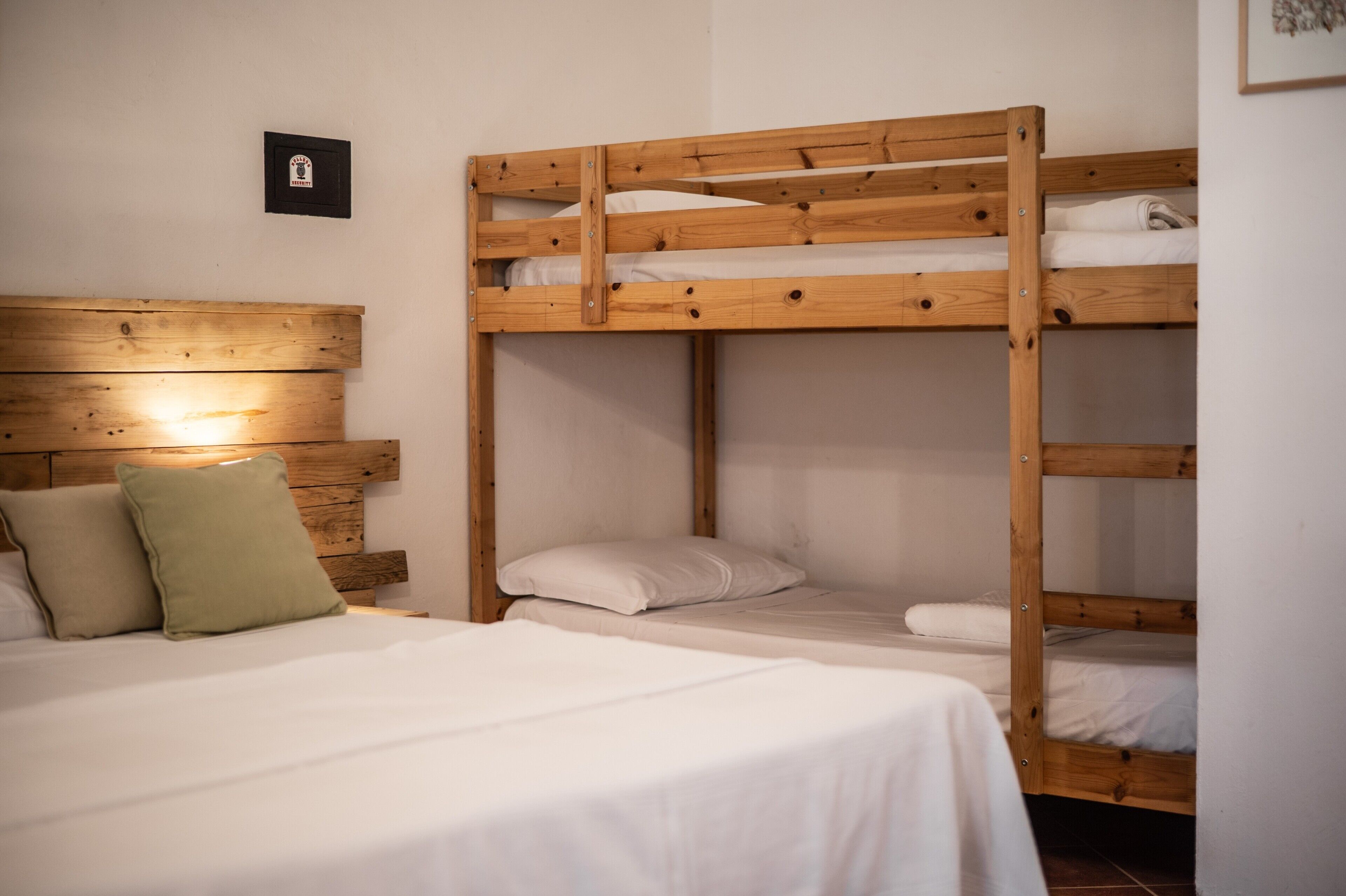 Une chambre avec un lit superposé doté d’une tête de lit en bois, un lit simple avec une literie blanche et un petit tableau encadré accroché au mur.