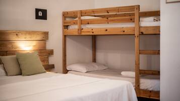 Une chambre avec un lit superposé doté d’une tête de lit en bois, un lit simple avec une literie blanche et un petit tableau encadré accroché au mur.