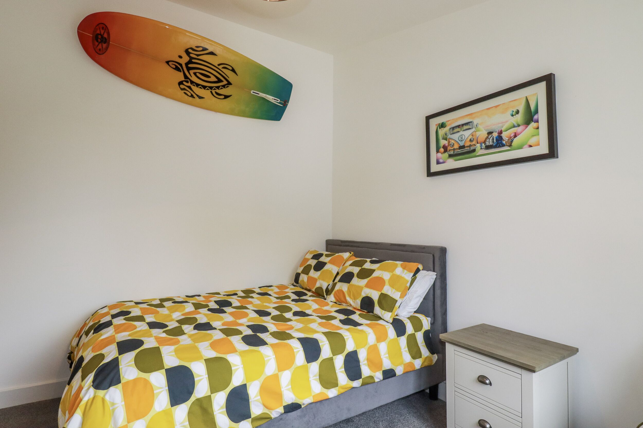 Une chambre à coucher avec un lit, une table de chevet, une planche de surf et un tableau accroché au mur.