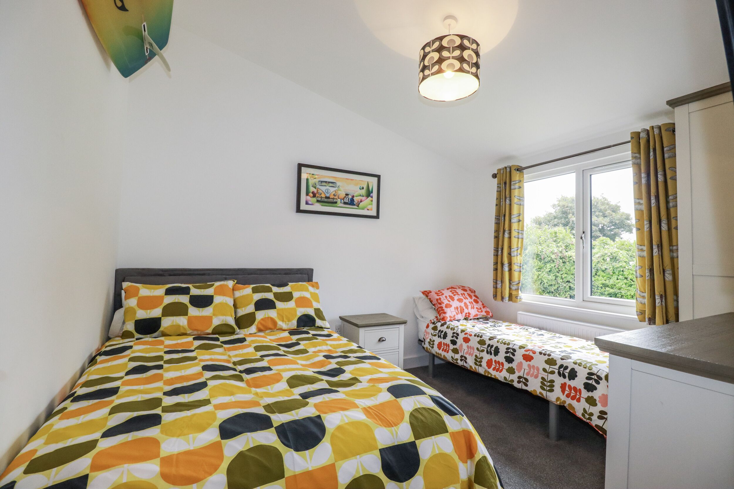 A bedroom with a bed, a bedside table, a window with curtains, and a picture on the wall.