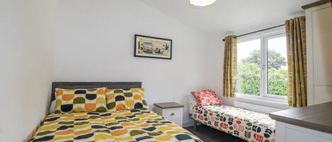 A bedroom with a bed, a bedside table, a window with curtains, and a picture on the wall.