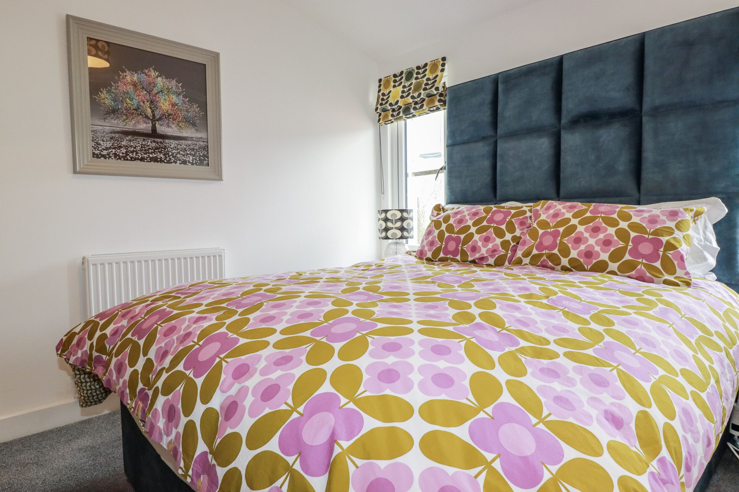 Une chambre à coucher avec un lit, une tête de lit, une fenêtre avec des rideaux et un radiateur.