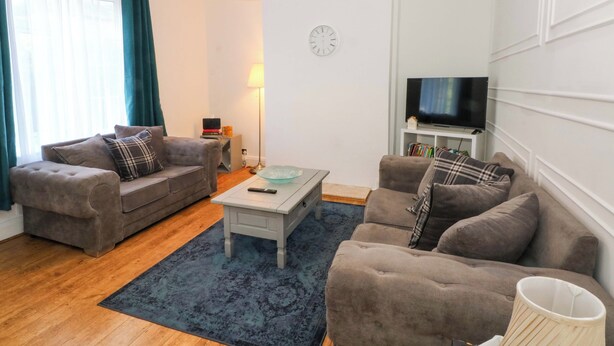 Ein Wohnzimmer mit zwei Sofas, einem Couchtisch, einem Fernseher und einer Uhr an der Wand.