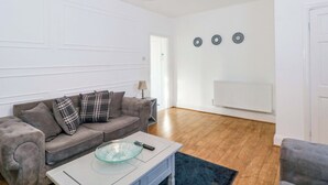 Ein Wohnzimmer mit grauem Sofa, einem Glastisch und einer pinkfarbenen Pendelleuchte.