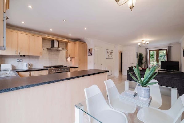 A modern kitchen with a central island, white dining chairs, and a flat-screen TV in the living area.
