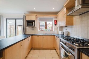 Een moderne keuken met houten kastjes, een gasfornuis, een magnetron en een raam met uitzicht op een achtertuin.