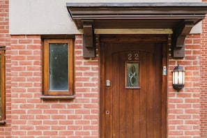 A brick building with a wooden door marked with the number 22, a window, and a wall-mounted light fixture.