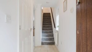 Un couloir avec un escalier recouvert de moquette, des murs blancs et une porte en bois.