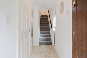 A hallway with a carpeted staircase, white walls, and a wooden door.