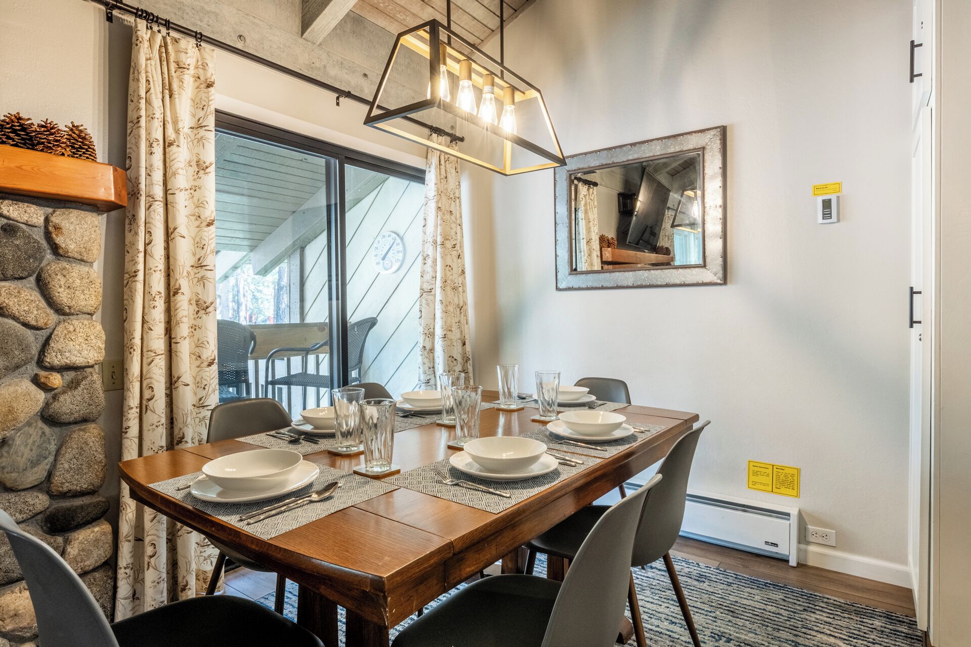 A dining area with a wooden table set for four, surrounded by stone walls and a large window.
