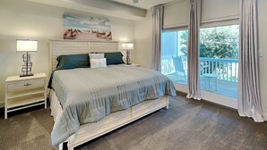 Een slaapkamer met een groot bed, twee nachtkastjes, een plafondventilator, een schilderij aan de muur en een balkon met gordijnen.