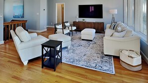 Een ruime woonkamer met een grote televisie, comfortabele zithoek en een decoratief vloerkleed.