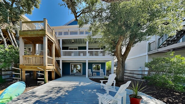 A wooden deck with outdoor seating, a tree, and a building with multiple balconies. - Shady Beaches by Topsail Realty (Holly Ridge)