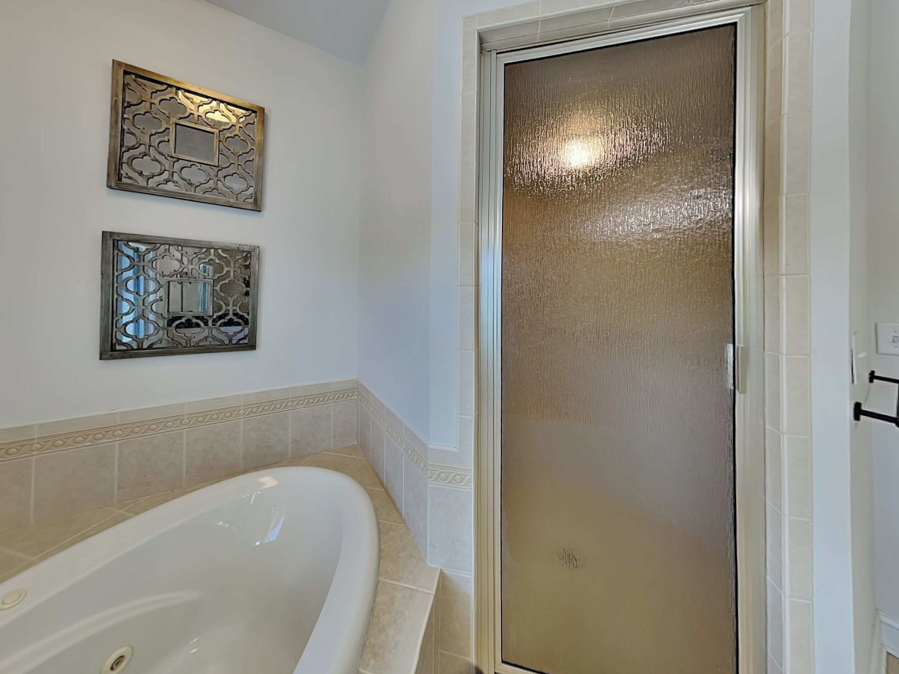 A bathroom with a bathtub, a frosted glass shower door, and decorative wall panels.