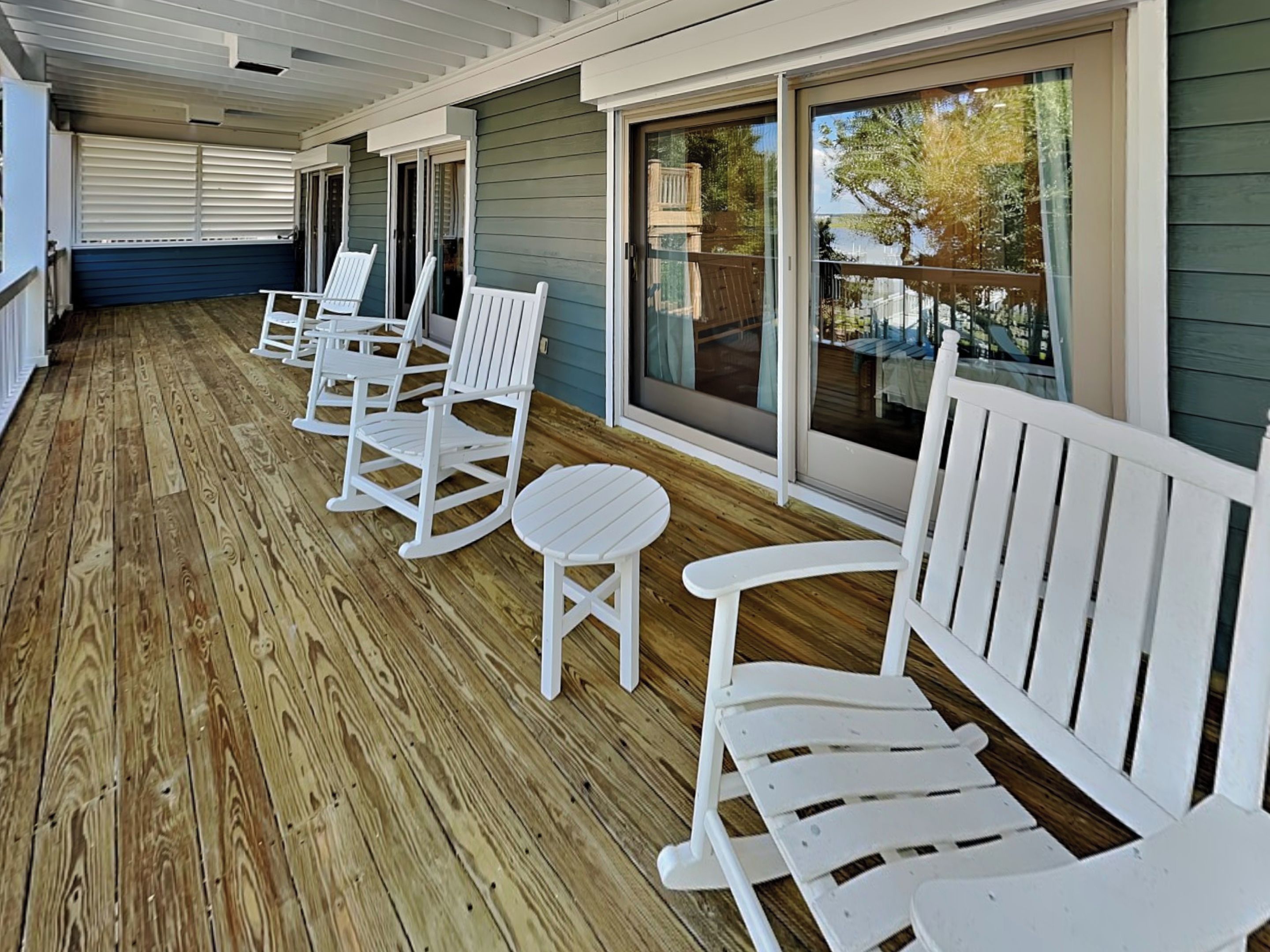 A covered porch with wooden flooring and white rocking chairs.