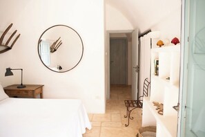 Ein Schlafzimmer mit einem Bett, einem Schreibtisch mit Lampe, einem runden Spiegel und einem Regal mit Dekoration.