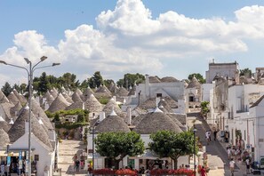 A street lined with traditional stone houses with conical roofs, a clear sky, and pedestrians.