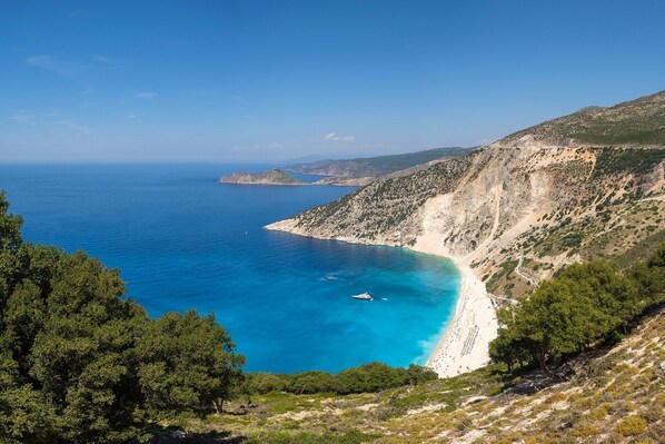 A coastal landscape with a beach, clear blue sea, and rocky cliffs.