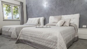 Une chambre avec deux lits, une fenêtre avec des rideaux, un plateau avec des tasses et une théière, et un mur gris à la texture particulière.
