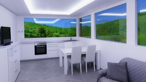 Une cuisine moderne avec un coin repas, de grandes fenêtres offrant une vue sur des collines verdoyantes et un téléviseur à écran plat.