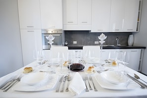 Une table à manger dressée avec de l’argenterie, des assiettes blanches et des verres à vin, avec une cuisine moderne en arrière-plan.