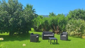 Un jardin aménagé avec du mobilier d’extérieur, comprenant un canapé, des fauteuils et une table, le tout entouré d’une végétation luxuriante et d’arbres.