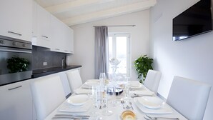 Une cuisine moderne avec des meubles blancs, une table à manger dressée pour six personnes, agrémentée de verres transparents, et un téléviseur à écran plat fixé au mur.