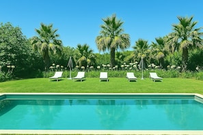Une piscine entourée de chaises longues blanches et de palmiers.