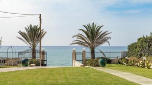 A coastal pathway leading to a gated entrance with palm trees and a view of the sea.