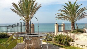 An outdoor patio with a table and chairs, palm trees, and a view of the sea.