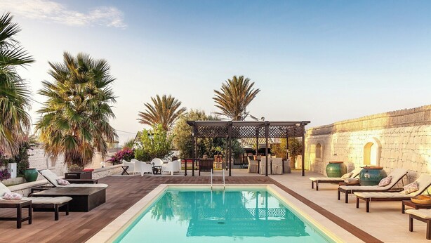 A rooftop pool area with lounge chairs, a pergola, and a stone wall.